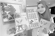  ??  ?? Pos Malaysia personnel Siti Farhana Md Jalil showing the national flower-themed stamp series. — Bernama photo