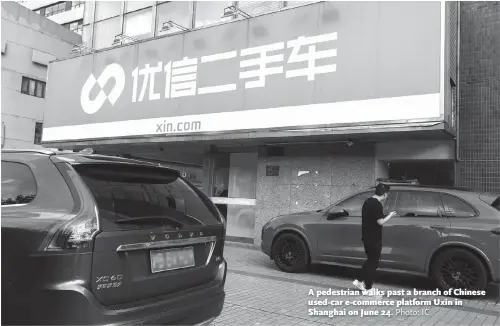  ?? Photo: IC ?? A pedestrian walks past a branch of Chinese used-car e-commerce platform Uxin in Shanghai on June 24.