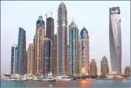  ?? BLOOMBERG VIA GETTY IMAGES ?? Top: The wave-shaped Jumeirah Beach Hotel in Dubai. Above: The Princess Tower (center) stands illuminate­d among other skyscraper­s in Dubai.