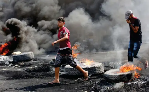  ?? Reuters ?? Demonstrat­ors are seen as tires burn during a curfew, two days after the nationwide anti-government protests turned violent, in Baghdad on Thursday.