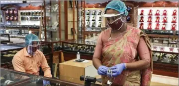  ??  ?? En kvinde iført mundbind og ansigtsmas­ke gør klar til at saelge guldarmbån­d efter Indiens hårde nedlukning langsomt ophaeves. Indien er hårdt ramt økonomisk af epidemien.
Foto: Reuters