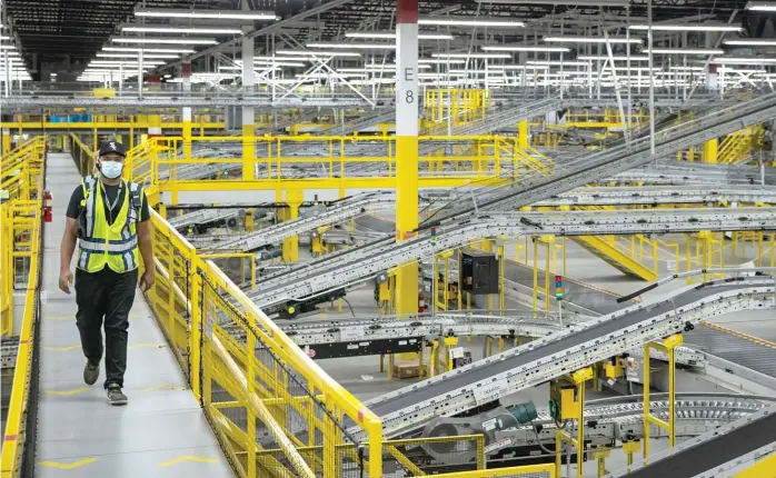  ?? ASHLEE REZIN GARCIA/SUN-TIMES ?? A worker on a catwalk at the Amazon MDW7 fulfillmen­t center in Monee. The massive facility is nearly a million square feet and contains about six miles of conveyors.