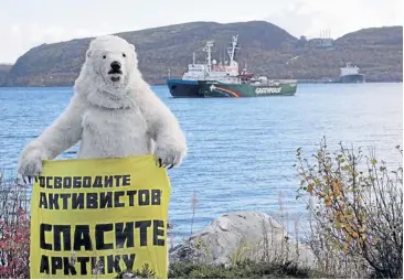  ?? AFP ?? A Greenpeace activist dressed as a polar bear holds a banner in front of the Arctic Sunrise, Greenpeace’s protest ship, moored next to a Russian Coast Guard ship, at the military base Severomors­k on the Kola peninsula near Murmansk. The poster reads...