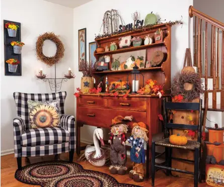  ?? ?? Yvonne combines warm and cool tones to great effect in her living room. The wood of an antique set-back hutch glows against the black elements showcased on and around it. “The hutch was an heirloom from my mother-in-law,”Yvonne notes. A wrought-iron floor lamp complement­s an oversize candle lantern and a shutter turned floral display featuring mini galvanized buckets.