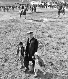  ??  ?? An Afghan man walking with children as horsemen compete in the traditiona­l sport of buzkashi on the outskirts of Kabul. — AFP photos