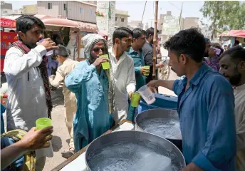  ?? — AFP photos ?? People drink water being distribute­d by volunteers along a street during a heatwave in Jacobabad.