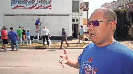  ?? ANGELA PETERSON / MILWAUKEE JOURNAL SENTINEL ?? Longtime Kenosha resident Jonathon Kim, owner of U.S. Taekwondo Academy on Sheridan Road, talks Monday about President Donald Trump visiting the city Tuesday and the current racial climate in the city. Behind him, students and supporters of his academy, which suffered $25,000 damage during the protests, gather to start a mural on the outside of the business. “I teach my students that Kenosha will bounce back,” he said.