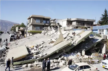  ??  ?? People gather around a leveled building in the mountainou­s town of Darbandikh­an in Iraqi Kurdistan following a 7.3-magnitude quake that hit the Iraq-Iran border area. (AFP)