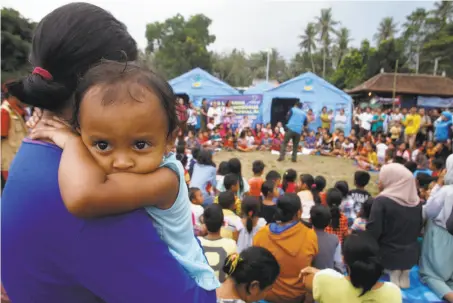  ?? Trisnadi / Associated Press ?? A woman carries her baby at a shelter for villagers who fled their homes on the slope of Mount Agung in Karangasem, Bali.