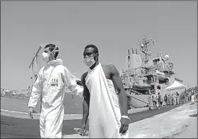  ?? AP/MAX FRIGIONE ?? An Italian paramedic escorts a migrant Friday during the disembarkm­ent of 402 migrants from a British navy ship in the harbor of Brindisi, Italy.