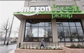  ?? – AP ?? New service: An Amazon worker returning with a cart after loading a bag of groceries into a customer’s car at an AmazonFres­h Pickup location in Seattle.