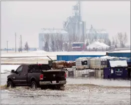  ?? HERALD PHOTO IAN MARTENS ?? A pickup truck drives over a flooded section of road next to bins surrounded by water Monday at Wilson Siding, as Lethbridge County declared a state of local emergency due to flooding in low drainage areas.