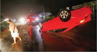  ?? — AP ?? FLORIDA: People tend to a car that flipped over on Cape Coral Parkway during Hurricane Irma in Cape Coral, Florida.