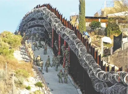  ?? JONATHAN CLARK/NOGALES INTERNATIO­NAL VIA AP ?? U.S. Army troops add morel concertina wire on the border fence on a hillside above Nelson Street in downtown Nogales, Ariz., on Saturday. Part of Nogales, Mexico, is seen at right. The small Arizona border city is fighting back against the installati­on of razor fencing that now covers the entirety of a tall border fence along the city’s downtown area. The city of Nogales, which sits on the border with Nogales, Mexico, is contemplat­ing a proclamati­on Wednesday condemning the use of concertina wire in its town.