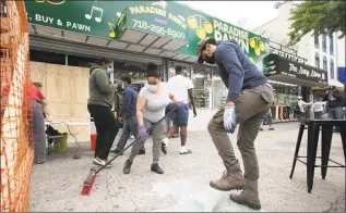  ?? Mark Lennihan / Associated Press ?? Natalie Colon, left, an employee with Paradise Pawn, is helped by community volunteer Jode Santana to clean up broken glass windows Tuesday in the Fordham Road area of the Bronx borough of New York. Protesters broke into the store Monday night in reaction to George Floyd's death while in police custody on May 25 in Minneapoli­s.