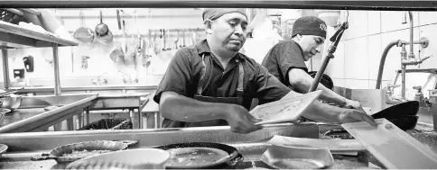  ??  ?? Dishwasher­s Soc, left, and Aguilar take turns rinsing, sorting and moving dishes through the conveyor-type machine, and then sorting them on a steel table at Caracol in Houston, on July 12.