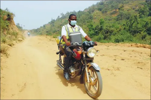  ?? ?? Yunusa Bawa, a community health worker, rides on a motorbike Monday with a box of AstraZenec­a covid-19 vaccine in Sabon Kuje on the outskirts of Abuja, Nigeria. (AP/Gbemiga Olamikan)