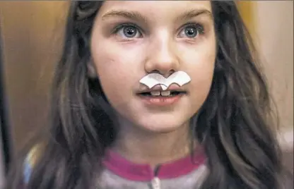  ??  ?? Keeley Ashbaugh uses a torn heart sticker to make a mustache as she plays with her stepsister­s in February at their home in North Vandergrif­t. Keeley now lives with her father, who is in recovery, her stepmother and a combined family of three sisters....