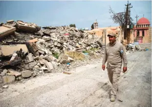  ??  ?? QARAQOSH: A member of the Nineveh Plain Protection Units (NPU), a small Christian militia charged with protecting the predominan­tly Christian Iraqi town of Qaraqosh (Hamdaniya), walks past demolished houses in the town which lies some 30 kilometers...