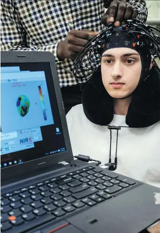  ?? JEFF MCINTOSH/THE CANADIAN PRESS ?? University of Calgary bio-medical engineerin­g student Ibukun Oni adjusts a headcap worn by Carter Randall unveiling new technology developed by the university to detect and monitor concussion­s. The device acts as a portable brain-imaging system.