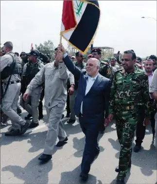  ?? THE ASSOCIATED PRESS ?? This image posted on the official Facebook account of Iraq’s Prime Minister Haider al-Abadi shows the premier carrying the national flag as he walks with Iraqi security forces in Tikrit, Iraq, on Wednesday.