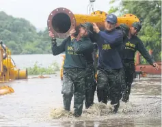  ??  ?? Soldiers carry unused water pipes and machinery to higher ground following the Kaeng Krachan dam spillover.