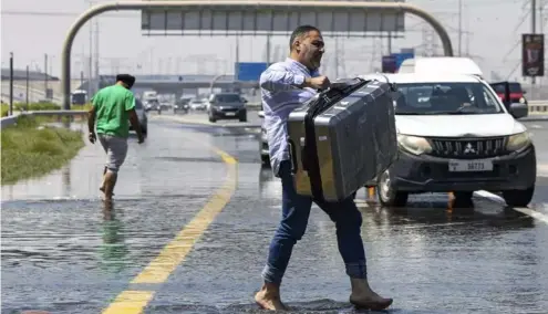  ?? ?? A man carries luggage through   oodwater caused by heavy rain while waiting for transporta­tion in Dubai, United Arab Emirates on Thursday