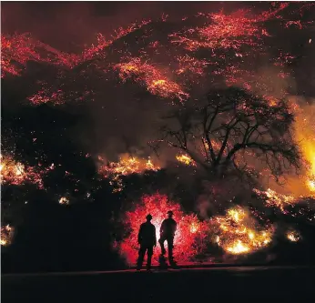  ?? MARIO TAMA / GETTY IMAGES ?? Firefighte­rs monitor a section of a wildfire along the 101 freeway on Thursday north of Ventura, Calif. Strong Santa Ana winds are rapidly pushing multiple wildfires across the region.