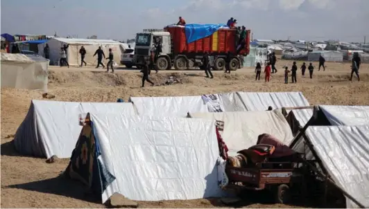  ?? ?? ► Palestinos en un campamento mientras llega un camión con ayuda humanitari­a en Rafah, cerca de la frontera con Egipto.