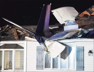  ?? Sarah Gordon / Associated Press ?? A plane is seen smashed into the roof of a home following a crash on Aug. 17 in Groton. The small plane crashed into the home while en route to a local airport Monday night, but the pilot, a passenger and a man in the house escaped serious jury, state and local officials said.