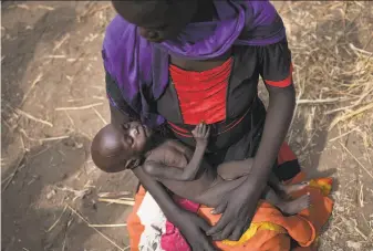  ?? Associated Press ?? A woman cradles her 10-month-old daughter at a food distributi­on site in the Ghazal region. South Sudan no longer has areas in famine, but 2 million people are on the brink of starvation.