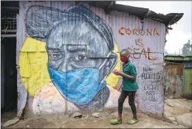  ?? (AP/Brian Inganga) ?? A boy carries a bowl of mixed beans and maize Saturday as he walks past an informatio­nal mural warning people about the risk of the coronaviru­s in the Mathare slum of Nairobi, Kenya. The mural was painted by graffiti artists from the Mathare Roots youth group.