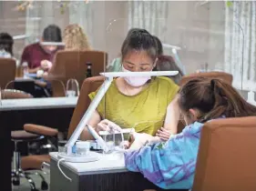  ?? ARIEL COBBERT/THE COMMERCIAL APPEAL ?? A nail salon employee works on a customer through a plexiglass shield at Elite Nail Spa in Germantown on Tuesday.