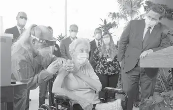  ?? MARTALAVAN­DIER/AP ?? Gov. Ron DeSantis watches Dec. 16 as nurse Christine Philips, left, gives a vaccine to Vera Leip at John Knox Village, in Pompano Beach. Nursing home residents and health care workers in Florida began receiving the Pfizer vaccine.