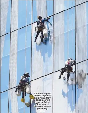  ?? REUTERS ?? Laborers rappel down a high-rise building as they clean glass windows in Makati City’s central business district
yesterday.