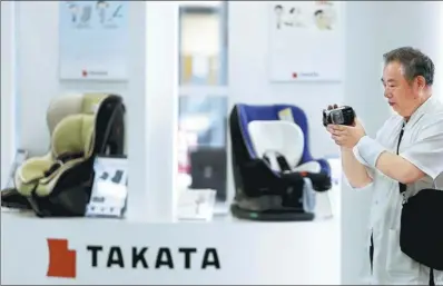  ?? REUTERS ?? A visitor holding a video camera stands next to a logo of Takata Corp on its display at a showroom for vehicles in Tokyo, Japan. Ningbo Joyson Electronic Corp is on a shortlist of candidates to rescue Takata.