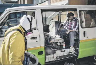  ?? Picture: AFP ?? A taxi driver, right, eats breakfast in his van as Steven Smith, a Scientolog­y volunteer minister, prepares to spray the vehicle with disinfecta­nt at the Bree Street Taxi Rank in Newtown yesterday.