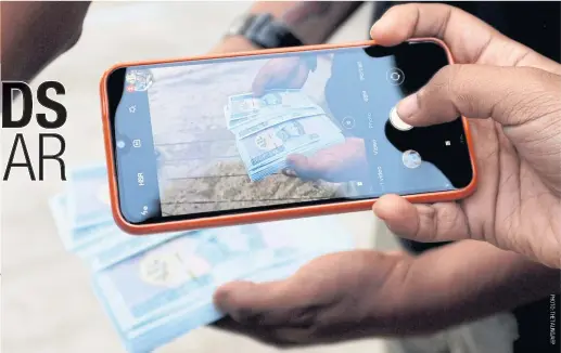  ??  ?? A man takes a picture of new kyat banknotes bearing a portrait of the late general Aung San, outside the Myanmar Economic Bank in Nay Pyi Taw.