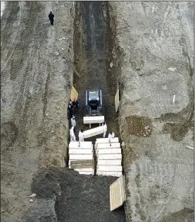  ?? (AP/John Minchillo) ?? Workers bury bodies Thursday in a trench on Hart Island at a public cemetery in the Bronx borough of New York that is used mainly for dead people who aren’t claimed or whose families can’t afford funerals. Under a new policy, the city has shortened the time it will hold unclaimed bodies, and an aerial check Thursday showed about 40 caskets lined up for burial.