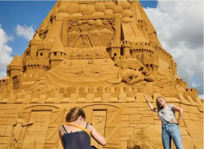  ?? — Reuters ?? Tourists take photos in front of the world’s tallest sandcastle in Blokhus, Denmark, on Wednesday. It stands over 20 meters high.