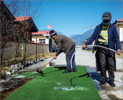  ?? PALDEN NYIMA / CHINA DAILY ?? Two villagers clean an artificial lawn in Bupal, a resettleme­nt site for impoverish­ed people in Zayul county, Tibet autonomous region.