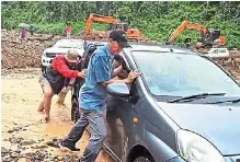  ?? ?? Easing the process: Kiulu assemblyma­n datuk Joniston Bangkuai (in red) helping to push a car that was trapped in the mud following a landslide at the Bayaon area along Jalan Kiulu-tamparuli.