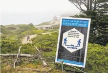  ??  ?? A sign encourages social distancing at the Golden Gate overlook in the Presidio. The busy parks around the Bay Area on the pleasant weekend made public health officials nervous.