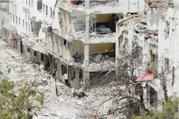  ?? — Reuters ?? People are seen next to buildings damaged at the scene where a car bomb exploded targeting a Mogadishu hotel in a business centre in Maka Al Mukarama street in Mogadishu.