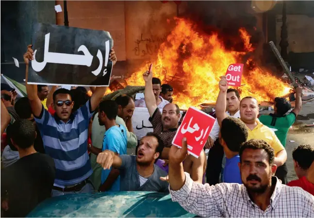  ?? HEBA KHAMIS / THE ASSOCIATED PRESS ?? Opponents of Egypt’s President Mohammed Morsi hold Arabic signs reading “leave,” as fire rages at the Muslim Brotherhoo­d headquarte­rs in Alexandria.