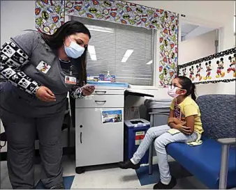  ?? ?? Jessica Sanchez, a licensed vocational nurse, checks patient informatio­n before administer­ing the Pfizer vaccine to Natalia Adame, 8, at the Kaiser Permanente medical office building Friday afternoon.