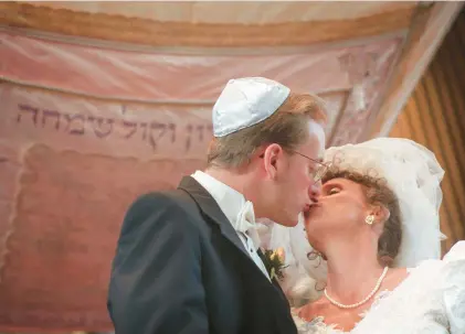  ?? TAMARA VONINSKI/VIRGINIAN-PILOT ?? A bride and groom kiss under a chuppah (a Jewish wedding canopy) after their wedding ceremony.