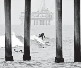  ?? MARK RALSTON, AFP/GETTY IMAGES ?? Surfers ride the waves in front of an oil rig off Huntington Beach, Calif.