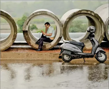  ??  ?? A motorist looks at his mobile as he sits inside a pipe amid heavy rainfall in New Delhi on Wednesday.