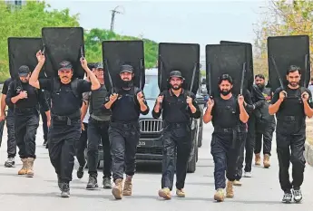  ?? AFP ?? Security personnel with ballistic shields escort a vehicle carrying former prime minister ■ Imran Khan as he leaves after appearing in a court in Islamabad yesterday.